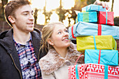 Young Couple Holding Stack of Christmas Presents Outdoors