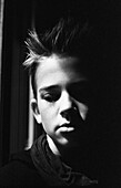 Kopf-Schulter-Porträt eines nachdenklichen Teenagers mit Blick nach unten, Gesicht teilweise im Schatten