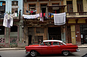 Cuba,Havana,an old red American car of the 50s passes by decrepit houses where clothes dry