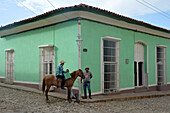 Kuba,Trinidad,ein Mann reitet auf einem Pferd und unterhält sich mit seinen Freunden vor einem grünen Kolonialhaus in einer gepflasterten Straße
