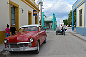 Kuba,Gibara,ein altes rotes amerikanisches Auto aus den 50er Jahren wird geparkt und ein alter Seitenwagen kommt in der gleichen Straße an
