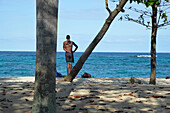 Kuba,Baracoa,Maguana beach,,homme,ein Mann ohne Hemd steht auf einem Baumstamm mit Blick aufs Meer