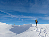 Austria,Tyrol,a man alone carrying a yellow backpack is hiking with touring skis in a white snowy landscape