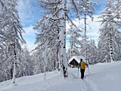Österreich,Tirol,ein Mann, der einen gelben Rucksack trägt, wandert in Richtung einer frisch verschneiten Holzhütte