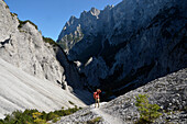 Austria,Styria,ENNSTAL Alps,Geseause national park,lynx trail , a man dressed in red carruing a backpack is standing on a mountain trail between the shade and the sun in direction to the Haindlkarh