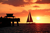 USA. Florida. Naples. Der Pier. Der Strand. Sonnenuntergang auf dem berühmten Pier. Touristen bewundern die Szene. Segelschiff.