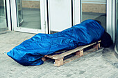 Homeless in a sleeping bag at the foot of a building