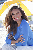 Woman in blue jumper and white trousers sitting on the beach