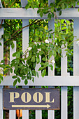 Weißer Holzzaun mit Rosen und Schild mit der Aufschrift "Pool"