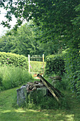 Holztor im Sommergarten, umgeben von üppigem Grün und Holzscheiten