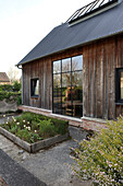 Modernes Holzhaus mit großen Fensterfronten und Hochbeeten im Vorgarten