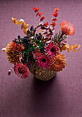 Herbstblumenstrauß mit Chrysanthemen (Chrysanthemum) und Eukalyptusblättern in geflochtenem Korb