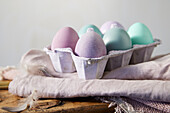 Pastel-coloured Easter eggs in egg carton on beige cloth