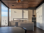 Modern kitchen with kitchen island and round dining area, wooden ceiling and large window front