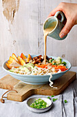 Hand pours dressing over bowl with pasta and fresh vegetables