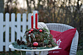 Adventsgesteck aus Zapfen mit roten Kerzen auf weißem Tisch im Garten