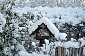 Snow-covered birdhouse next to wooden fence in winter garden