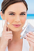 Young, dark-haired woman in a white swimsuit sprays herself with sunscreen