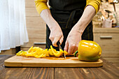 Woman slices yellow pepper on wooden board