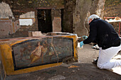 Archaeologist excavating fresco on ancient Roman food stand, Pompeii, Italy