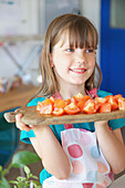 Lächelndes junges Mädchen hält Schneidebrett mit Tomaten