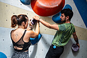 Young man teaching woman in her twenties how to climb on a climbing wall indoors