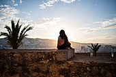 Junge Frau genießt den Sonnenuntergang von der Stadtmauer der Burg Papa Luna in Peñiscola, Castellon, Valencianische Gemeinschaft, Spanien