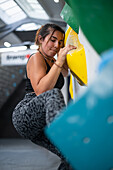 Young man in her twenties climbing on a climbing wall indoors