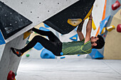 Junger Mann in den Zwanzigern beim Klettern an einer Kletterwand in einer Halle