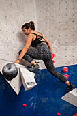 Young man in her twenties climbing on a climbing wall indoors