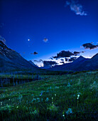 A nightscape scene under a twilight "blue-hour" sky, on the Red Rock Canyon Road in Waterton Lakes National Park, Alberta, looking west toward the sunset with the four-day-old crescent Moon setting alongside the stars of Leo to the left.