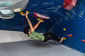 Junger Mann in den Zwanzigern beim Klettern an einer Kletterwand in einer Halle