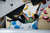 Junger Mann in den Zwanzigern beim Klettern an einer Kletterwand in einer Halle