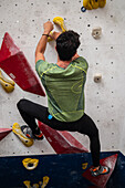 Junger Mann in den Zwanzigern beim Klettern an einer Kletterwand in einer Halle