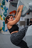 Young man in her twenties climbing on a climbing wall indoors