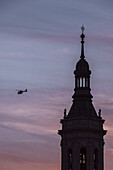 Helicopter flying next to one of the towers of the Cathedral-Basilica of Our Lady of the Pillar at sunset, Zaragoza, Spain