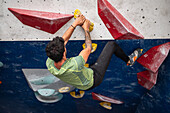 Young man in his twenties climbing on a climbing wall indoors