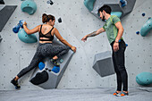 Young man teaching woman in her twenties how to climb on a climbing wall indoors