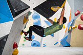 Young man in his twenties climbing on a climbing wall indoors