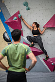 Young man teaching woman in her twenties how to climb on a climbing wall indoors