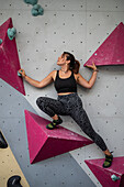 Young man in her twenties climbing on a climbing wall indoors