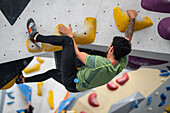 Junger Mann in den Zwanzigern beim Klettern an einer Kletterwand in einer Halle