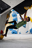 Junger Mann in den Zwanzigern beim Klettern an einer Kletterwand in einer Halle