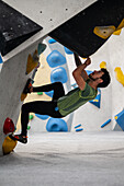 Junger Mann in den Zwanzigern beim Klettern an einer Kletterwand in einer Halle