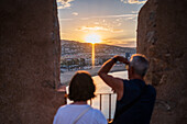 Ein Paar genießt den Blick auf den Sonnenuntergang von der Stadtmauer der Burg Papa Luna in Peñiscola, Castellon, Valencianische Gemeinschaft, Spanien