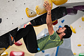 Junger Mann in den Zwanzigern beim Klettern an einer Kletterwand in einer Halle