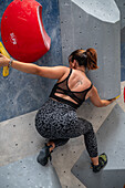 Young man in her twenties climbing on a climbing wall indoors