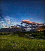 A nightscape scene under a moonlit sky, on the Red Rock Canyon Road in Waterton Lakes National Park, Alberta, looking back along Pass Creek to the south, with the Milky Way rising at left. Waterton is a UNESCO World Heritage site.