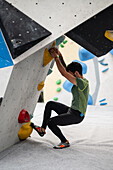 Young man in his twenties climbing on a climbing wall indoors