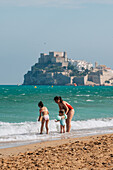 Familie am Strand und Blick auf die Burg Papa Luna in Peñiscola, Castellon, Valencianische Gemeinschaft, Spanien